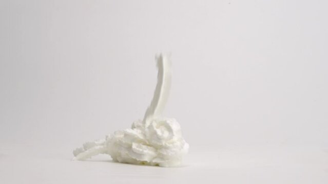 Ribbons of white whipped cream topping falling into pile on white table top and being drizzled with rich brown chocolate syrup for perfect ice cream sundae topping in slow motion