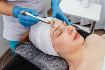 Woman in spa having a facial treatment. Special electric equipment for skincare. Beautiful woman face receiving facial microcurrent treatment with apparatus from therapist in beauty wellness salon