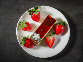 Three chocolates cake with chocolate drips on a black background. Layered cake with milk, black and white chocolate souffle decorated with strawberries on top. Confectionery background with copy space