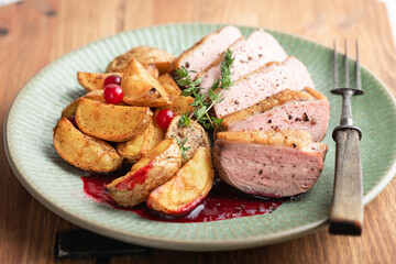Roasted duck breast with potatoes and berry sauce on wooden background, selective focus, close-up