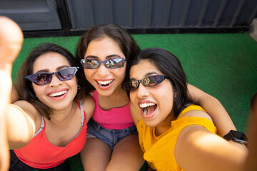 Portrait of three indian friends fun girls wearing sunglasses and colorful outfit taking photos...