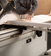 The carpenter cutting the parts from chipboard on a circular saw at a furniture factory.
