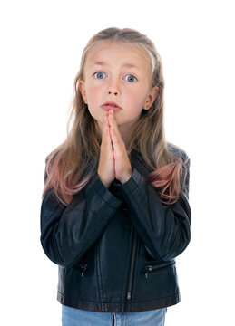 Portrait of regretful five year old girl looks gloomy and desperate, keeps palms together, beggs for forgiveness. Cute blondy child in black leather jacket and blue jeans in studio on white background