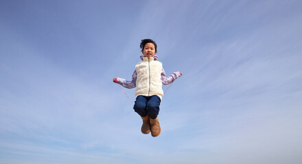 冬の屋外で高く跳んで縄跳びを遊んでいる小学生の女の子の様子