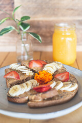Peanut butter, banana and strawberry toast on a table with fresh juice and coffee.