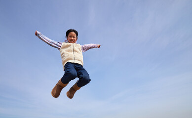 Fototapeta na wymiar 冬の青空と元気で空にジャンプしている小学生の女の子の様子