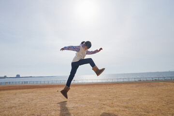 Fototapeta na wymiar 冬の海岸の公園で元気で跳んで遊ぶ小学生の女の子の様子
