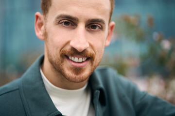 Fototapeta premium Closeup portrait happy handsome bearded entrepreneur looking at camera and smiling while posing outdoors. Positive lifestyle concept