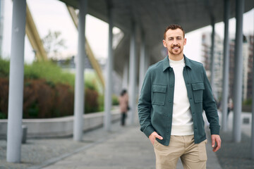 Happy tourist man looking at camera and walking at street, copy space. Smiling guy enjoying positive lifestyle  outdoors. Vacation, travel concept 