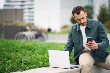 University student studying online using laptop and smartphone while sitting in university campus, copy space. Online education concept  