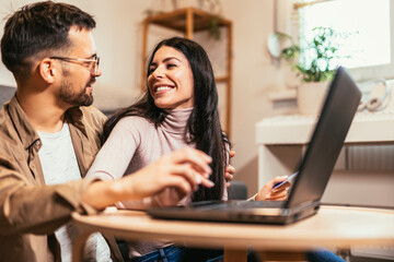 Fototapeta premium Happy young couple shopping together, customers paying by credit card online, sitting in cozy living room at home