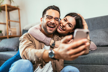 Beautiful young loving couple bonding to each other and making selfie while sitting on the couch together