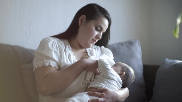 Madre sentada amamantando a bebé desde su pecho en posición de cuna viendo a su hijo tomando leche materna