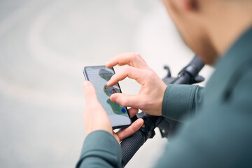 Cropped view of the man hands swiping mobile app while preparing riding scooter at the street, selective focus. Transportation and technology concept