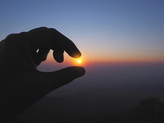 Silhouette of Hand picking sun at sunrise sky