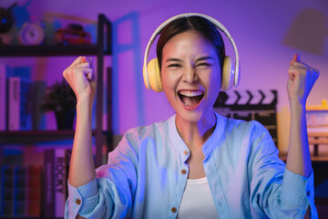 Young Asian woman wearing headset and hand raises arms and fists clenched with shows strong...