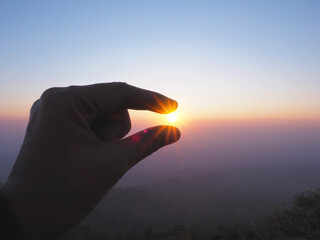 Silhouette of Hand picking sun at sunrise sky - 569080462