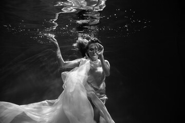 Young beautifull caucasian woman in dress under water in black and white