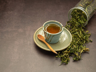 Obraz na płótnie Canvas Dry cannabis leaf tea outside a box and marijuana tea cup on a table