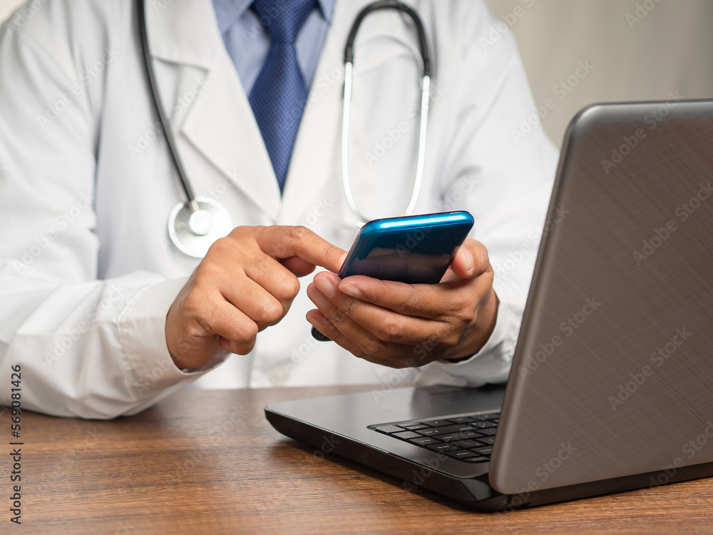 Poster doctor in a uniform with a stethoscope using a smartphone while sitting at the desk