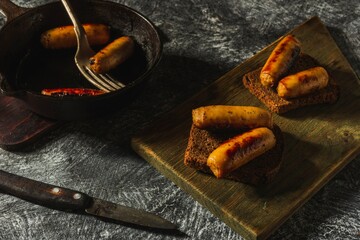 Still life in a rustic style- fried sausages in a cast-iron pan on a dark background