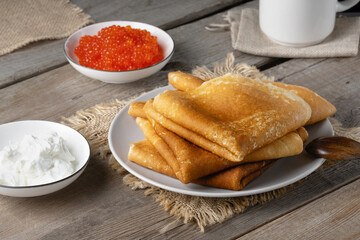 Stack of russian thin pancakes blini with red caviar and fresh sour cream