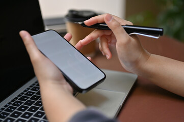 Close-up image a businesswoman holding pen and using her smartphone while working