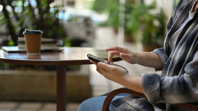 Close-up side view image of a hipster woman sits at cafe outdoor seat using her smartphone.