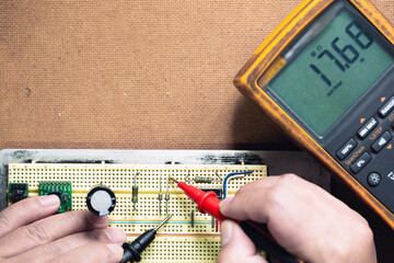 hand holding multimeter probe and measuring at electronics device on the board