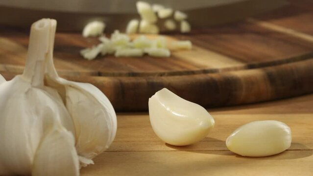  garlic on a wooden chopping board close-up. a knife grinds a clove of garlic surrounded by whole ones. kitchen on a sunny day. High quality photo