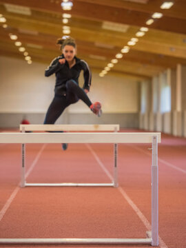 Female runner jumping hurdles on tartan track at athletics hall, Offenburg, Baden-W&uuml;rttemberg, Germany