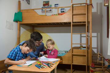 Brothers colouring with coloured pencils while father is assisting them, Munich, Germany