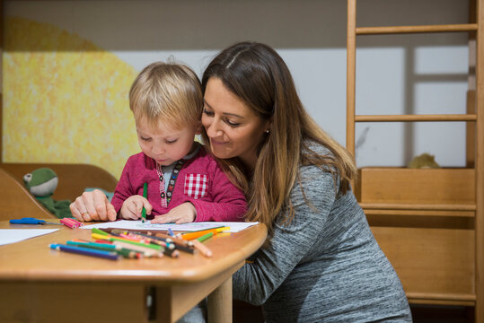 Mother assisting son to draw with coloured pencil, Munich, Germany