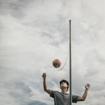 Asian Teen Boy Plays Tetherball Against a Stormy Sky