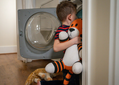 Young boy putting stuffed tiger into the washing machine