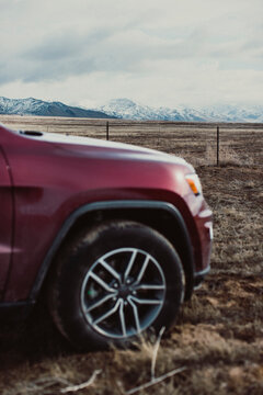 A red SUV is pulled off the side of road next to mountains.