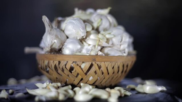 Shot of garlic bulbs in a wicker basket on black wooden surface, garlic in wooden basket  HD footage.
