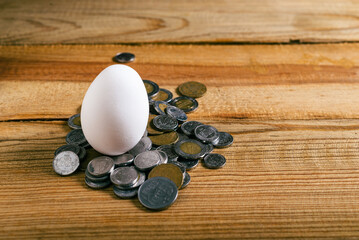 Egg and pile of Mexican coins on wooden table. Concept of rising cost of egg production and...