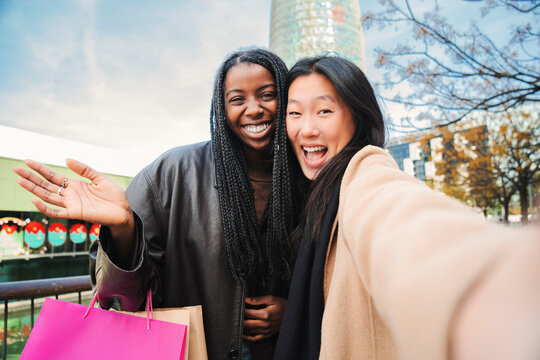 Close Up Portrait Of Two Happy Young Women Doing A Selfie Portrait Looking At Camera. Front View Of A Couple Of Multiracial Girls Smiling And Having Fun Taking A Photo. One Asian Lady And Her African