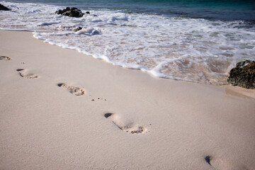 Texture background Footprints of human feet on the sand beach near turquoise sea water.