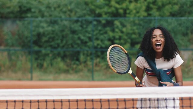 4k video. Young and beautiful sporty african american woman playing tennis in clay court. Amatour frienship match. Vintage and retro racket. Natural tree background.