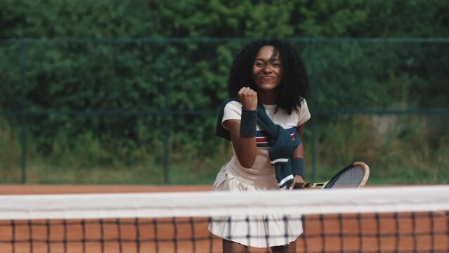 4k video. Young and beautiful sporty african american woman playing tennis in clay court. Amatour frienship match. Vintage and retro racket. Natural tree background.