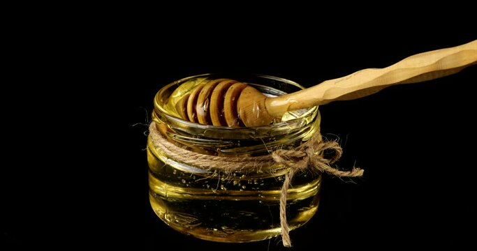 Honey flows down from a spoon spindle into a jar with honey on a black background.