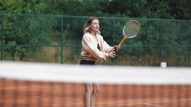 4k video. Young and beautiful sporty blonde woman playing tennis in clay court. Amatour frienship match. Vintage and retro racket. Natural tree background.