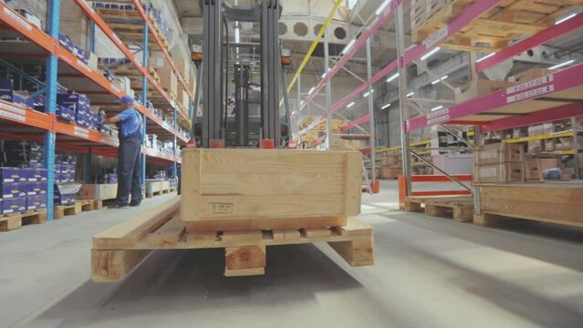 A forklift carries a wooden box. A forklift with cargo rides through the warehouse