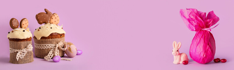 Delicious Easter cakes with eggs, chocolate candies and bunny on lilac background. Banner for design