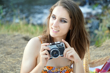 Portrait of a beautiful young woman having picnic outside in nature wearing summer dress and photographing with vintage film camera