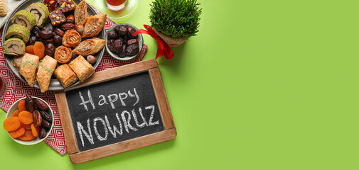 Chalkboard with text HAPPY NOWRUZ, sweets and wheat grass on green background with space for text