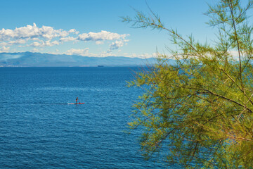 Fototapeta premium Unrecognizable person stand-up paddle boarding at Adriatic sea Kvarner gulf seen from the Lovran town coastline