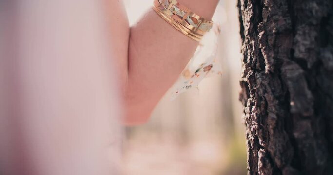 Cropped image of a woman's arm with gold jewelry and a gold foil temporary tattoo resting on a tree trunk in a forest in Slow Motion